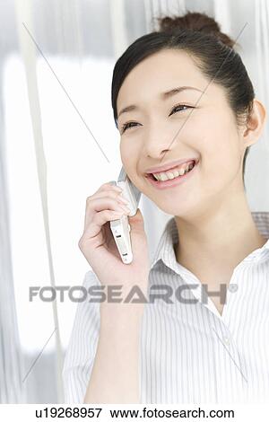 Stock Photo - Woman smiling and using mobile phone, front view. Fotosearch