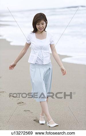 Stock Photo - A Smiling Young Woman Walking on the Beach, Front View. Fotosearch