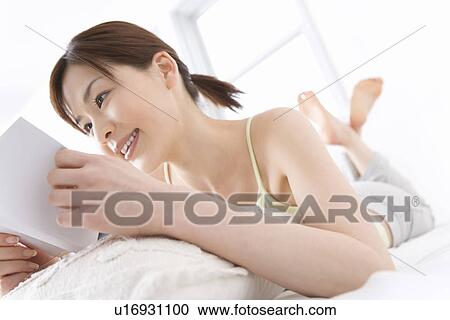 Stock Image - A Young Woman Lying on Her Stomach and Reading a Book, Low Angle View. Fotosearch