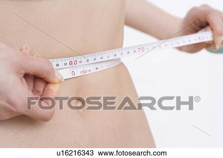 Stock Image - A Young Woman Measuring Her Waist, Close Up, No Face, Differential Focus. Fotosearch