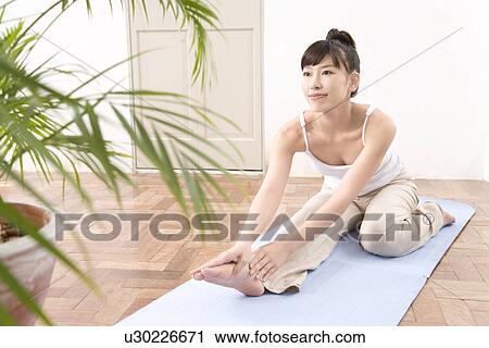 Stock Image - A Young Woman Practicing Yoga, Stretching Legs, Side View. Fotosearch