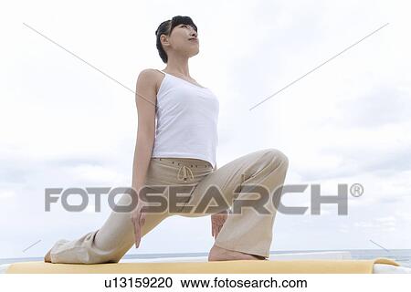 Stock Image - A Young Woman Stretching at Beach, Low Angle View. Fotosearch