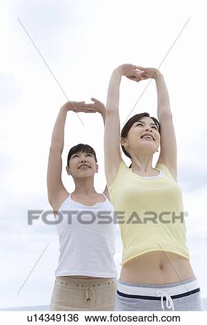 Stock Photograph - Two Young Women Stretching, Arms Up in the Air, Low Angle View. Fotosearch