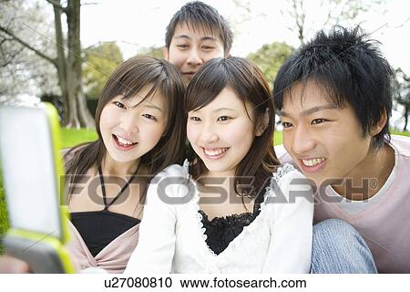 Stock Image - Four young people looking at mobile phone, front view, Japan. Fotosearch