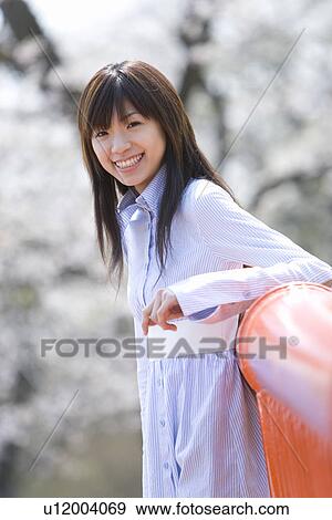 Portrait of a young woman leaning on a railing, smiling and looking at camera, side view, differential focus, Japan View Large Photo Image Stock Photo - Portrait of a young woman leaning on a railing, smiling and looking at camera, side view, differential focus, Japan. Fotosearch