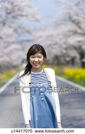 Portrait of a young woman on road lined with cherry trees, smiling and looking at camera, front view, Japan View Large Photo Image Stock Image - Portrait of a young woman on road lined with cherry trees, smiling and looking at camera, front view, Japan. Fotosearch