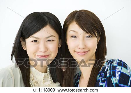 Stock Photo - Portrait of two women smiling and looking at camera, front view, white background, Japan. Fotosearch