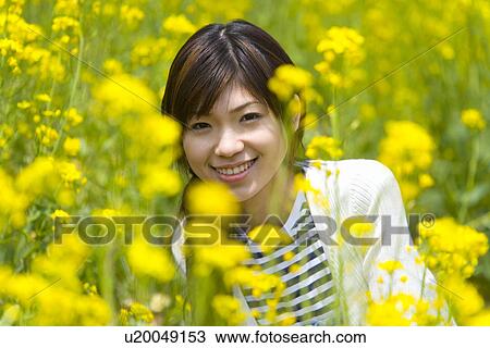 Stock Image - Portrait of woman in rape field, smiling and looking at camera, front view, Japan. Fotosearch