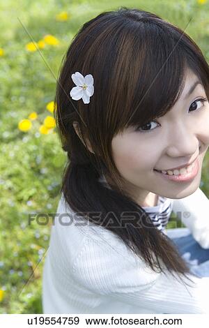Stock Photo - Portrait of woman smiling and looking at camera, cherry flower on her hair, high angle view, Japan. Fotosearch
