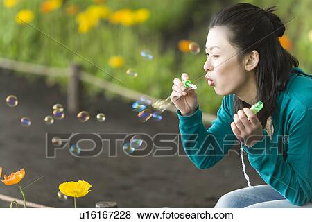 Stock Photo - Woman blowing soap bubbles, side view, Japan. Fotosearch