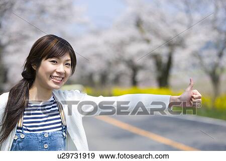 Stock Photo - Woman hailing on side of road lined with cherry trees, front view, Japan. Fotosearch