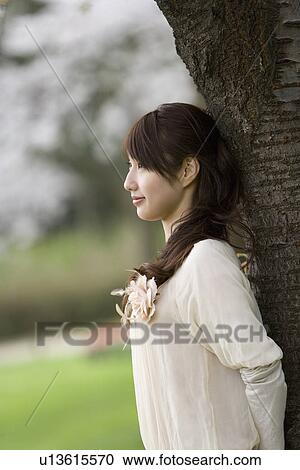 Stock Image - Woman leaning on tree trunk, side view, Japan. Fotosearch