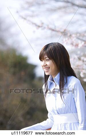 Stock Photo - Woman smiling and standing under the cherry trees, side view, Japan. Fotosearch