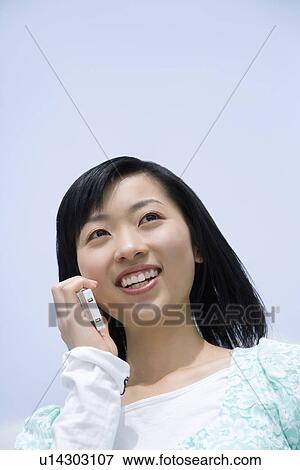 Stock Photo - Woman using a mobile phone under the blue sky, low angle view, blue background, Japan. Fotosearch
