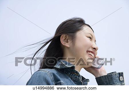 Stock Photograph - Woman using a mobile phone under the blue sky, low angle view, side view, blue background, Japan. Fotosearch