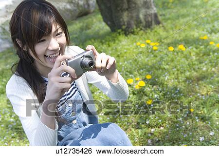 Young Woman smiling and holding a digital camera on lawn, front view, Japan View Large Photo Image Stock Photograph - Young Woman smiling and holding a digital camera on lawn, front view, Japan. Fotosearch
