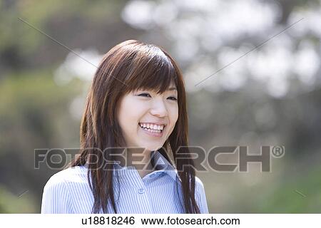 Stock Photograph - Young woman smiling, front view, differential focus, Japan. Fotosearch