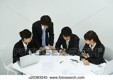 Stock Photography - Four young business people in meeting, high angle view, white background, Japan. Fotosearch