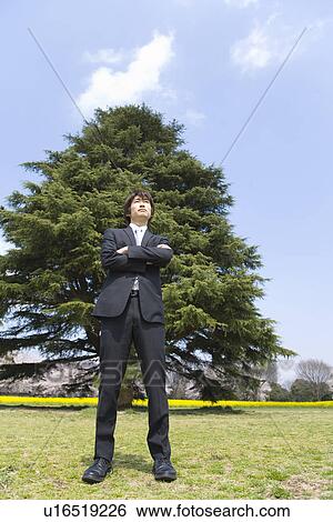 Stock Photograph - Man standing with arms crossed in the field, low angle view, Front View, Japan. Fotosearch