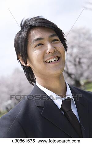 Stock Photography - Portrait of a man in the field of cherry blossoms, smiling, front view, Japan. Fotosearch