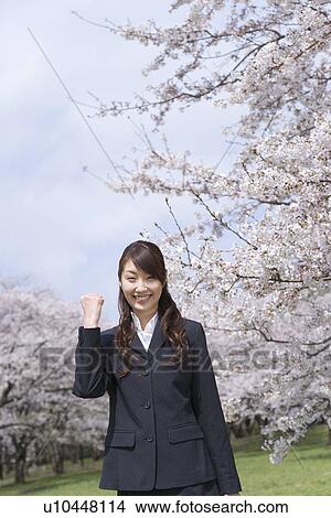 Picture - Portrait of a woman standing at the field of cherry blossoms, smiling and looking at camera, front view, Japan. Fotosearch