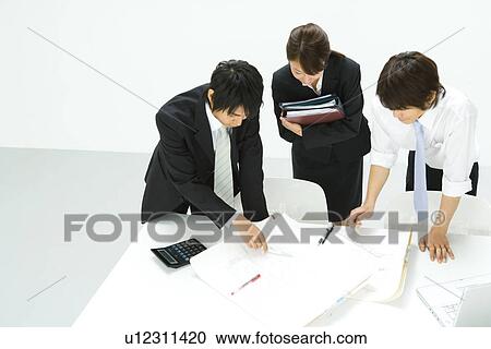 Stock Image - Three young business people in meeting, high angle view, white background, Japan. Fotosearch