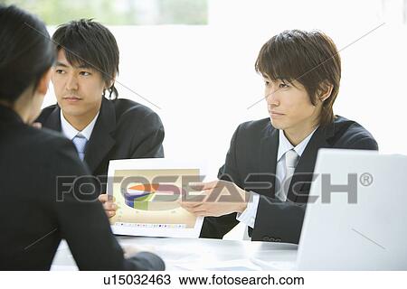 Stock Image - Three young business people in meeting, front view, rear view, Japan. Fotosearch