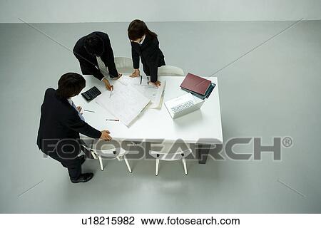 Stock Image - Three young business people in meeting, high angle view, white background, Japan. Fotosearch