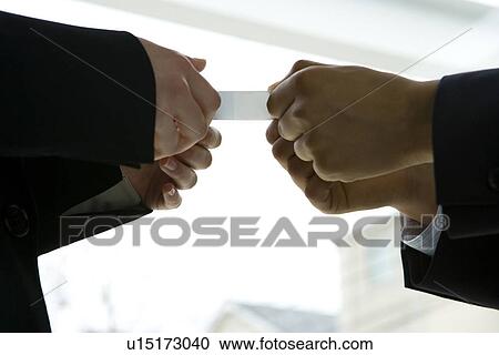 Stock Image - Two businessmen exchanging a business card, low angle view, side view, close up. Fotosearch