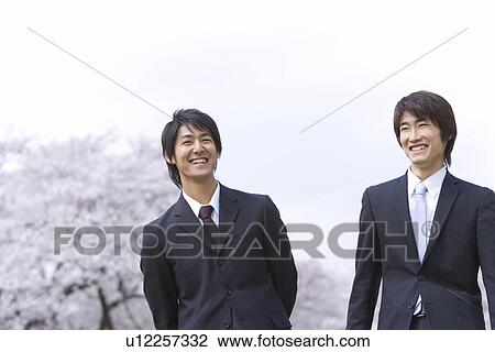 Stock Image - Two men in the field of cherry blossoms, smiling, front view, Japan. Fotosearch