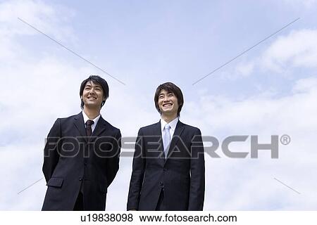 Stock Photo - Two men standing side by side under the blue sky, low angle view, Japan. Fotosearch