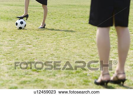 Stock Image - Two women playing soccer in the field, front view, rear view, Japan. Fotosearch