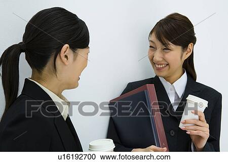 Two young businesswomen smiling and talking, holding paper cups, front view, side view, white background, Japan View Large Photo Image Stock Image - Two young businesswomen smiling and talking, holding paper cups, front view, side view, white background, Japan. Fotosearch