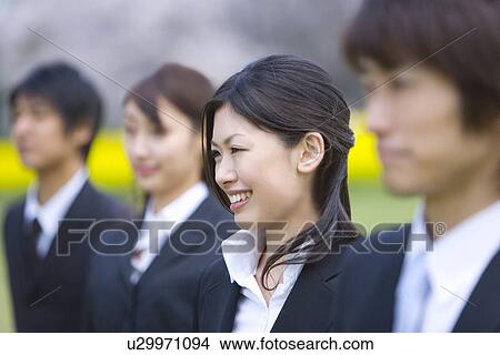 Picture - Young business people standing in a line side by side, side view, differential focus, Japan. Fotosearch