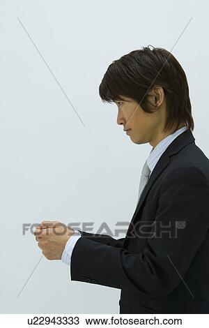Stock Image - Young businessman holding a business card, side view, white background. Fotosearch