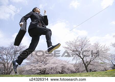 Picture - Young businessman jumping at the field of cherry blossoms, low angle view, Japan. Fotosearch