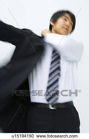 Stock Image - Young businessman putting jacket on, front view, white background, blurred motion, Japan. Fotosearch
