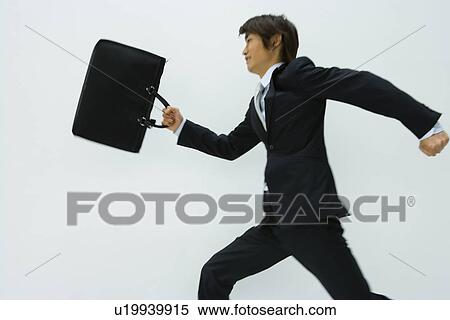 Stock Photography - Young businessman running and holding briefcase, side view, white background, Japan. Fotosearch