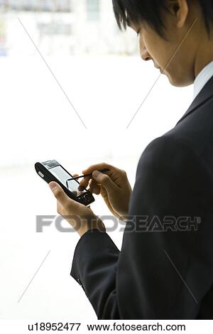 Stock Photo - Young businessman using a PDA, side view. Fotosearch