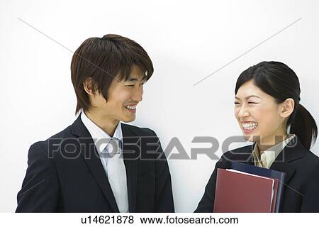Stock Photo - Young businesswoman and businessman smiling and talking, woman holding files, front view, white background, Japan. Fotosearch