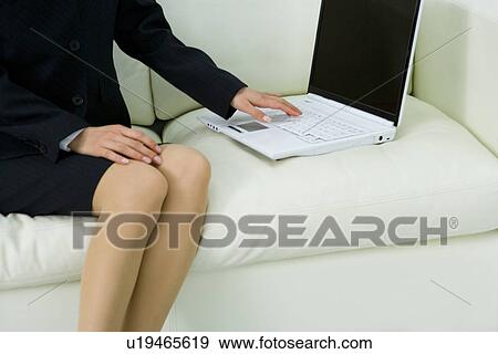 Stock Photo - Young businesswoman sitting on couch and using laptop, front view, Japan. Fotosearch