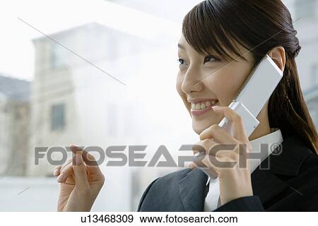 Stock Photo - Young businesswoman using mobile phone, side view, Japan. Fotosearch