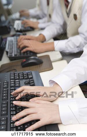 Stock Photography - Four teenagers using personal computers in library, side by side, side view. Fotosearch