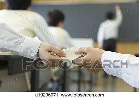 Stock Image - High school students exchanging memo during class, side view, rear view. Fotosearch