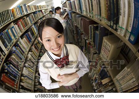 Stock Photograph - Portrait of a teenage girl holding a book in library, smiling and looking at camera, high angle view, side view, fish-eye lens. Fotosearch