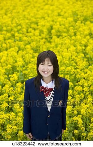 Stock Image - Portrait of a teenage girl standing in rape field, smiling and looking at camera, high angle view, Japan. Fotosearch