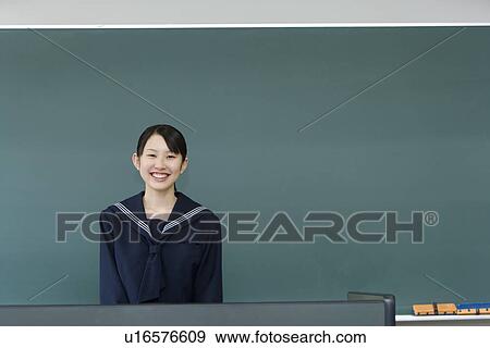 Stock Photo - Portrait of a teenage girl standing in front of blackboard, smiling and looking at camera, front view, copy space. Fotosearch