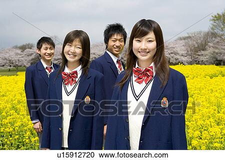 Stock Image - Portrait of four teenagers in rape field, smiling and looking at camera, front view, Japan. Fotosearch