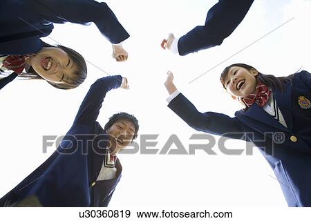 Stock Photo - Portrait of four teenagers punching the air, smiling and looking at camera, low angle view, white background, Japan. Fotosearch