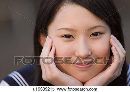 Stock Photography - Portrait of teenage girl resting head in hands, smiling and looking at camera, front view. Fotosearch